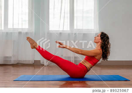 A young woman in a red tracksuit doing exercises or yoga in the gym. Serious, calm and focused slender girl. The concept of a healthy lifestyle. 89325067