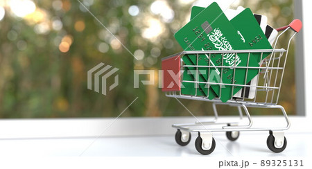 Bank card mockups with flags of Saudi Arabia in a small shopping cart. Conceptual 3D rendering 89325131