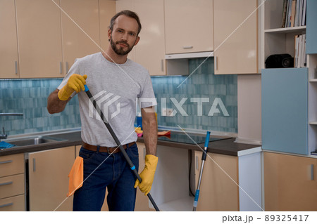 Young caucasian man in yellow rubber gloves holding mop Young caucasian man in yellow rubber gloves holding mop 89325417