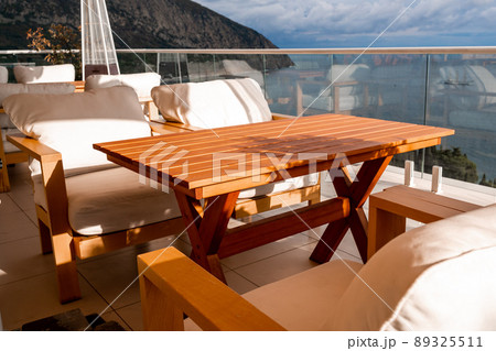 Restaurant with sea view. You can see rocks in the sea. Wooden tables and chairs with white cushions. Overcast, cloudy weather. Restaurant with sea view. You can see rocks in the sea. Wooden tables and chairs with white cushions. Overcast, cloudy weather. 89325511