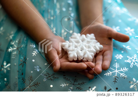 Winter and Christmas concept. Children's hands close-up holding a magic snowflake on the background of a blue dress with snowflakes. 89326317