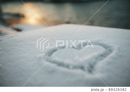 A heart symbol painted on fresh white snow against a sunset background. 89326382