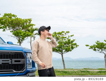 海岸沿いの駐車場で、青い車で待ち合わせをする若い男性 89328169