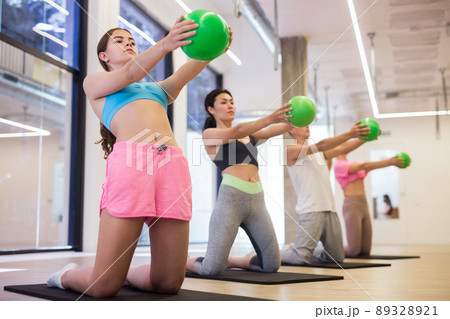 Sports people perform an exercise holding a mini Pilates ball in front of them Sports people perform an exercise holding a mini Pilates ball in front of them 89328921