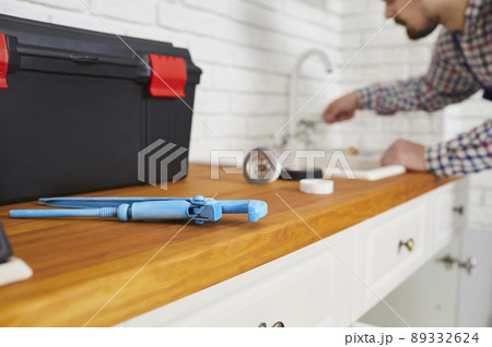 Plumber using a wrench and other tools while repairing the sink tap in the kitchen 89332624