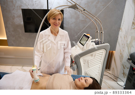 Hardware cosmetology. Young brunette woman getting rf lifting procedure in a beauty parlour. 89333364