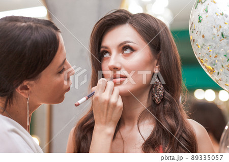 Young girl makeup artist paints lips of a beautiful girl with a lip liner. 89335057