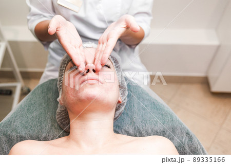 Doctor beautician makes cosmetic facial massage. Woman relaxes on a cosmetic chair.. 89335166