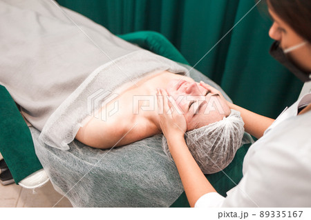 Doctor beautician makes cosmetic facial massage. Woman relaxes on a cosmetic chair.. 89335167