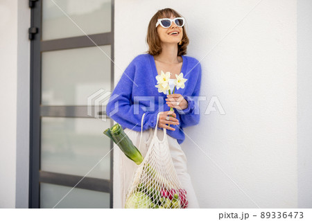 Woman with mesh bag full of fresh vegetables on porch of home 89336473