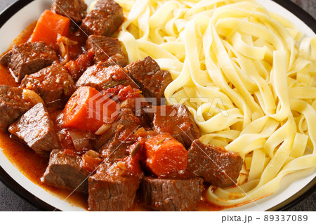 Slowly stewed spicy beef in red wine with vegetables served with noodles close-up in a plate. horizontal 89337089