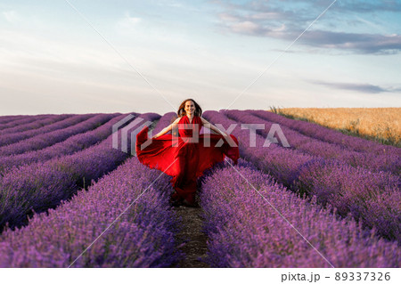 Among the lavender fields. A beautiful girl in a red dress runs against the background of a large lavender field 89337326