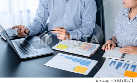 Two business colleagues pointing business data on laptop and taking notes information on notebook while reading 89338071