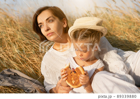 Mother and daughter sitting picnic high yellow grass child eat bun. 89339880