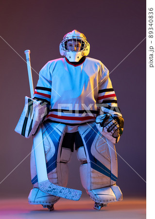 Portrait of boy, child posing in protective hockey uniform of goalkeeper isolated over purple background in neon light 89340836