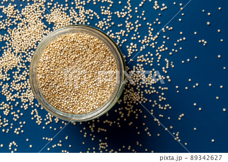 Raw quinoa in a glass jar and scattered grains over blue background. 89342627