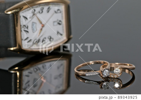 Pair of women's gold rings with diamonds on a background of elegant watches Pair of women's gold rings with diamonds on a background of elegant watches 89343925