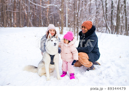 afro man with his caucasian wife having fun with a beautiful daughter playing husky in snowy park 89344479