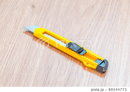 Yellow cutter knife with push button blade lock on wooden floor. Yellow cutter knife with push button blade lock on wooden floor. 89344773
