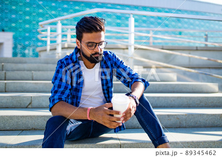 arabian man chelout with cocoa cup sits on stairs outdoors 89345462