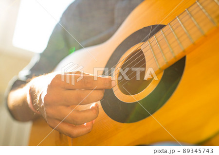 Cheerful handsome young man playing guitar and smiling in new cozy apartment Cheerful handsome young man playing guitar and smiling in new cozy apartment 89345743