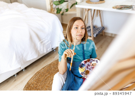 Woman artist holding paintbrush.Creative woman enjoying painting.Young beautiful woman in art studio, taking colorful paints from palette,creating masterpiece on easel, work, imagination Woman artist holding paintbrush.Creative woman enjoying painting.Young beautiful woman in art studio, taking colorful paints from palette,creating masterpiece on easel, work, imagination 89345947