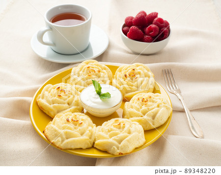 Diet cheese pancakes, rose shape, on yellow plate with tea, raspberry on textile linen napkin 89348220