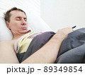 Man sleeping in bed with phone in his hands  89349854