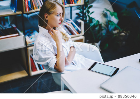 Pensive woman sitting in armchair at table 89350346