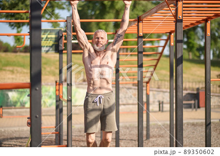 A gray-haired mature man having a workout on the open sports ground A gray-haired mature man having a workout on the open sports ground 89350602