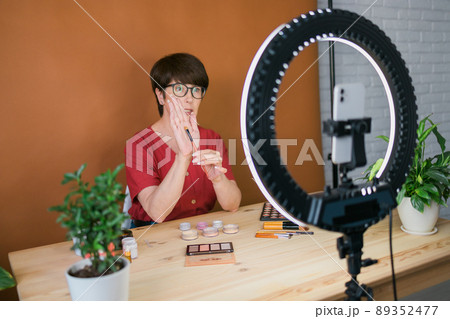 Beauty and cosmetics e-commerce and blogging concept - professional mature female make up artist testing new cosmetics recording video review on cosmetic products at home 89352477