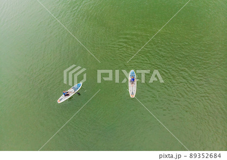 Strong men floating on a SUP boards in a beautiful bay on a sunny day. Aerial view of the men crosses the bay using the paddleboard. Water sports, competitions 89352684