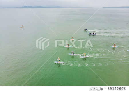Strong men floating on a SUP boards in a beautiful bay on a sunny day. Aerial view of the men crosses the bay using the paddleboard. Water sports, competitions Strong men floating on a SUP boards in a beautiful bay on a sunny day. Aerial view of the men crosses the bay using the paddleboard. Water sports, competitions 89352698