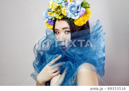 side view of sensual asian woman in floral hat with blue veil on neck posing on light grey background . indoor studio shot. 89353516