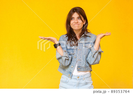 I don't know. Portrait of confused beautiful brunette young woman with makeup in denim casual style standing with raised arms, looking away and doubt. indoor studio shot, isolated on yellow background I don't know. Portrait of confused beautiful brunette young woman with makeup in denim casual style standing with raised arms, looking away and doubt. indoor studio shot, isolated on yellow background 89353764