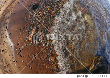 Directly Above Fisheye Shot Small Waves Rolling into Beach Dotted with Colorful Rocks and Pebbles Directly Above Fisheye Shot Small Waves Rolling into Beach Dotted with Colorful Rocks and Pebbles 89354144
