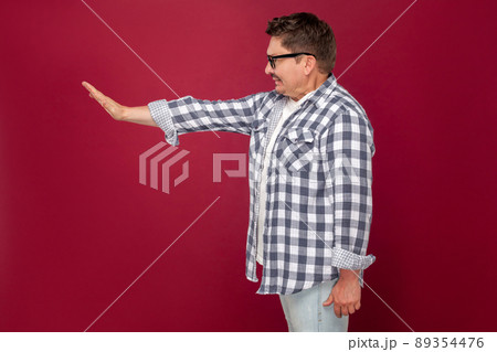 Profile side view portrait of angry handsome middle aged business man in casual checkered shirt and eyeglasses standing and showing stop with hand. indoor studio shot, isolated on dark red background. 89354476