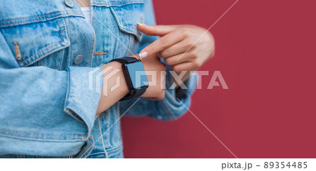 Closeup of woman hands in casual style with black smart watch pointing or touching and screen copyspace. indoor studio shot, isolated on red background. Closeup of woman hands in casual style with black smart watch pointing or touching and screen copyspace. indoor studio shot, isolated on red background. 89354485