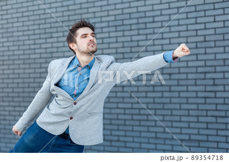 Profile side view portrait of serious handsome bearded man in casual style standing in superman gesture with fist and looking far. indoor studio shot on brick wall background. 89354718