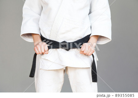 Female fighter torso poses in white kimono and sportive strong arms are closeup black belt. Japanese karate and sports concept. Indoor, studio shot, isolated, grey background 89355085