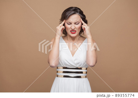 Woman unwell. Have headache and migraine. Emotion and feeling concept. Studio shot, indoor, isolated on light brown background Woman unwell. Have headache and migraine. Emotion and feeling concept. Studio shot, indoor, isolated on light brown background 89355774