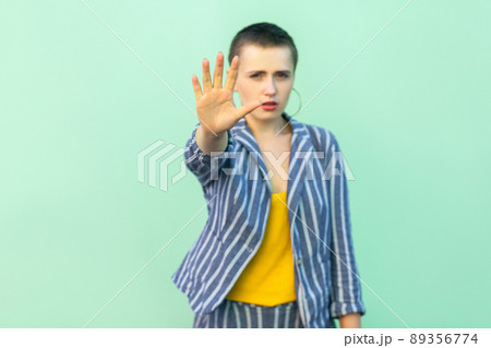 Stop. Portrait of serious handsome beautiful short hair young stylish woman in casual striped suit standing blocking and showing stop hand sign. indoor studio shot isolated on light green background. 89356774