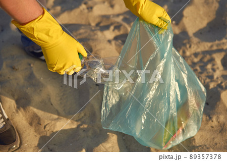 Young volunteer in yellow gloves is walking with garbage bag along a dirty beach of the river and cleaning up trash. People and ecology. Close-up. Young volunteer in yellow gloves is walking with garbage bag along a dirty beach of the river and cleaning up trash. People and ecology. Close-up. 89357378