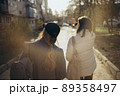 Back view portrait of two women walking and talking in a park asunny day 89358497