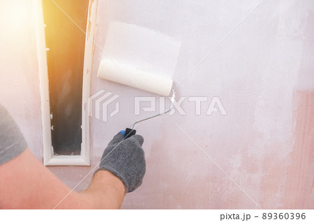 A man paints wooden door white. The painter uses a A man paints wooden door white. The painter uses a 89360396