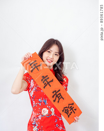 Young asian woman wearing traditional cheongsam qipao dress hold Chinese festival couplet to celebrate new year with word meaning "May there be surplus year after year" on white background. 89361785