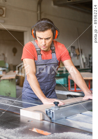 Woodworker cutting plank with table saw in workshop 89362214