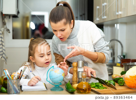 Mother cooking and little daughter doing school homework 89363464