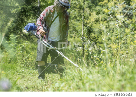 Man with protective headwear and goggles trimming the lawn 89365632