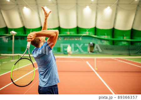 Instructor or coach teaching how to play tennis on a court indoor Instructor or coach teaching how to play tennis on a court indoor 89366357